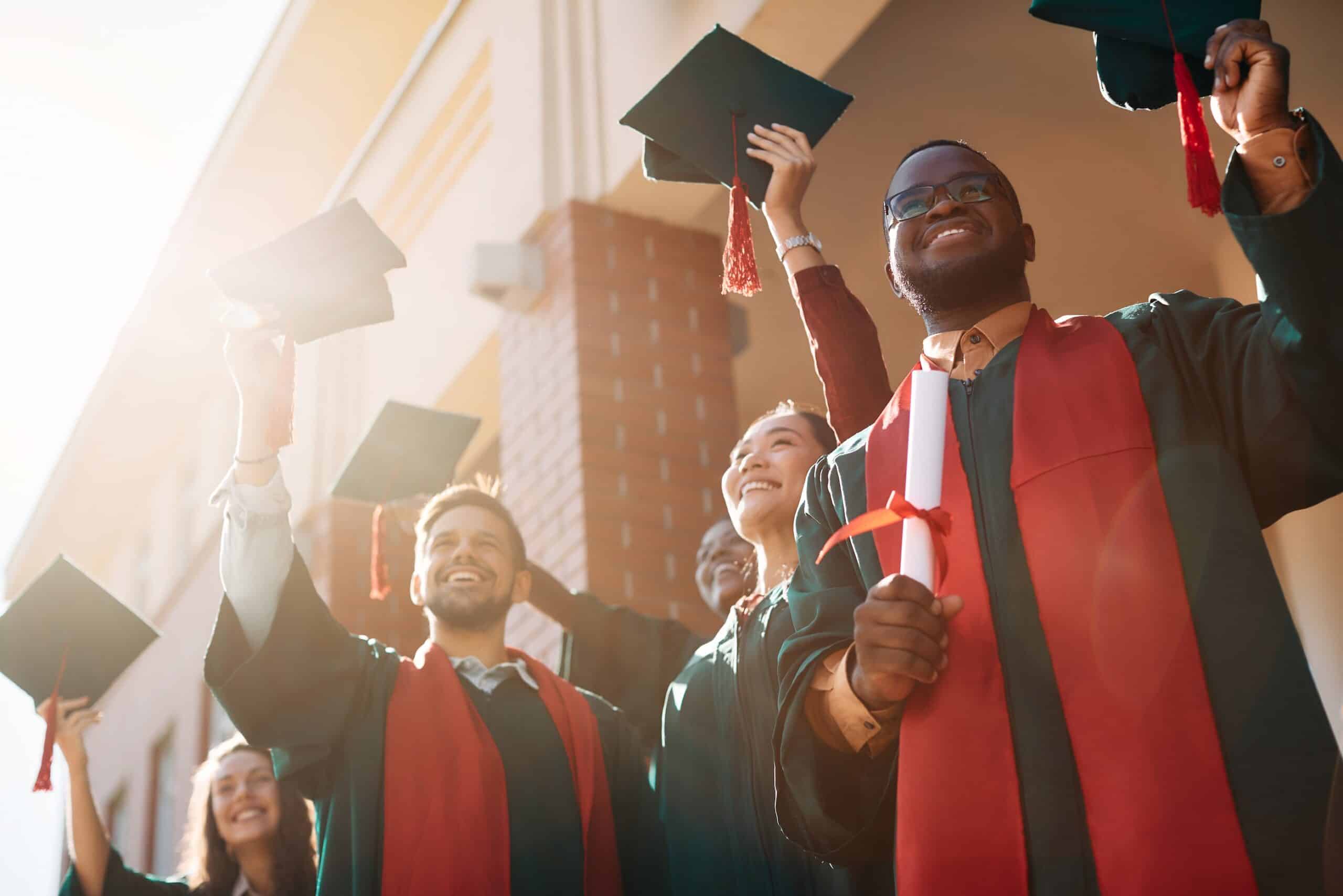 Happy multiracial college students celebrating after graduation ceremony at the university.
